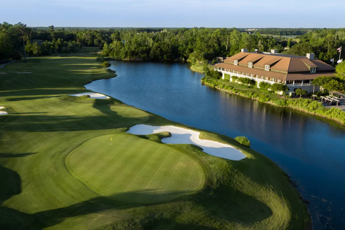 A sweeping view of the Azalea Sands Golf Club, with lush green fairways, well-kept sand traps, a sparkling water feature, and the inviting clubhouse visible. The bright, open landscape captures the essence of a classic golf getaway and invites viewers to imagine themselves teeing off under sunny Carolina skies.