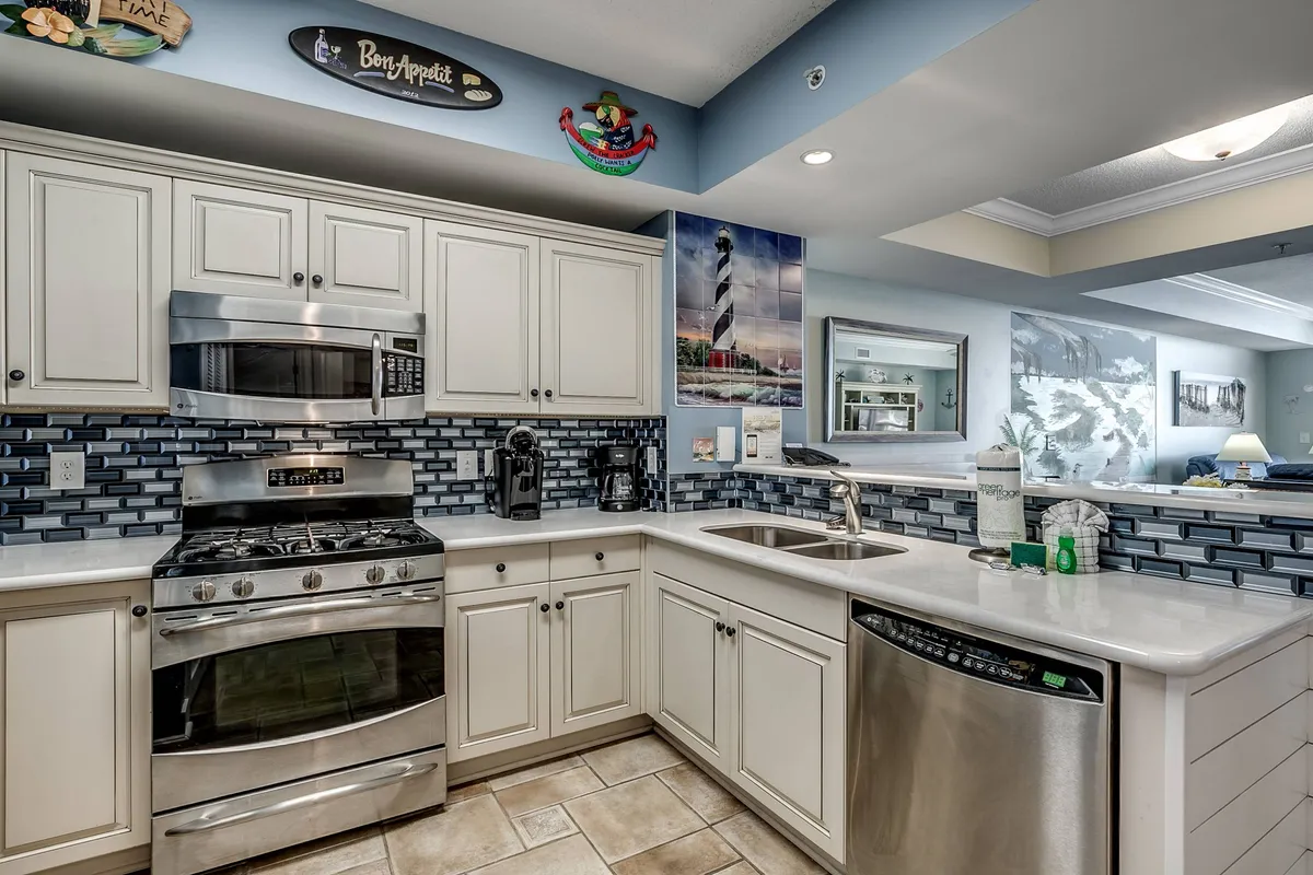 A bright, casual kitchen interior with stainless steel appliances, a blue backsplash, and decorative wall art. The layout invites both cooking and casual entertaining, perfect for families or small groups to prepare and enjoy meals together.