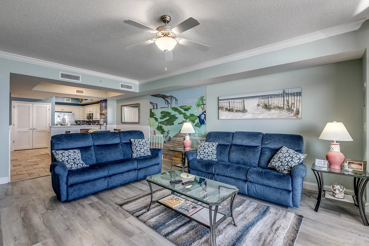 A cozy interior lounge area with blue couches, a glass coffee table, wall mural, and warm lighting, providing a comfortable space for guests to unwind, socialize, or enjoy a coffee in the morning and chats in the evening.